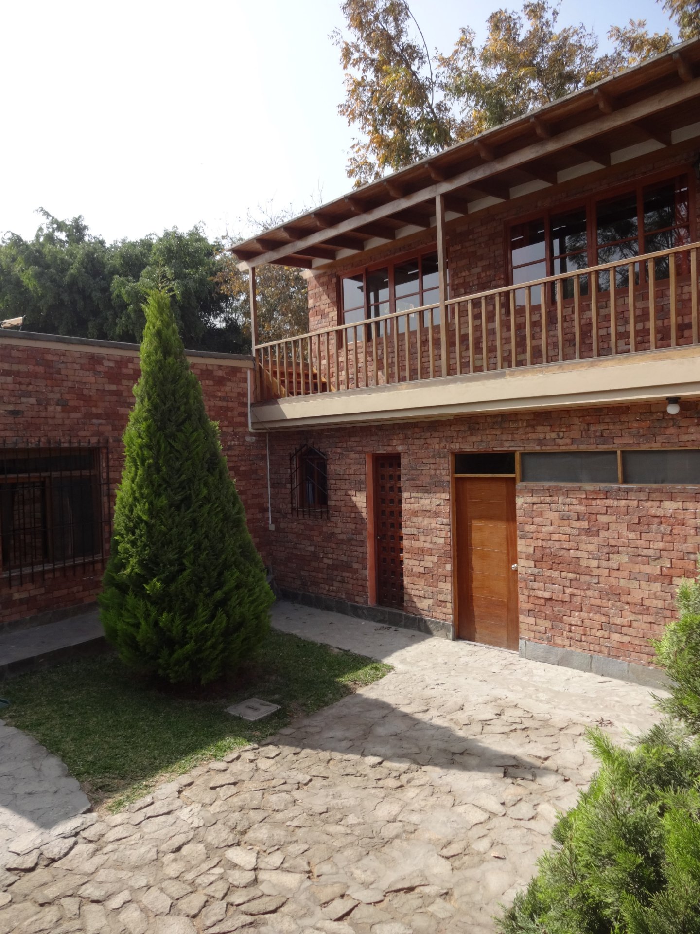 Enchape Antaño: casa de ladrillo con balcón y ciprés alto