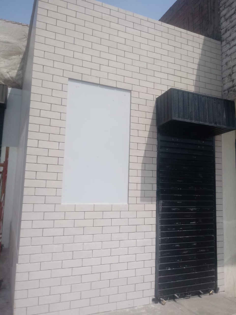 Enchape Blanco Humo: fachada de local comercial con enchape claro y puerta metálica negra